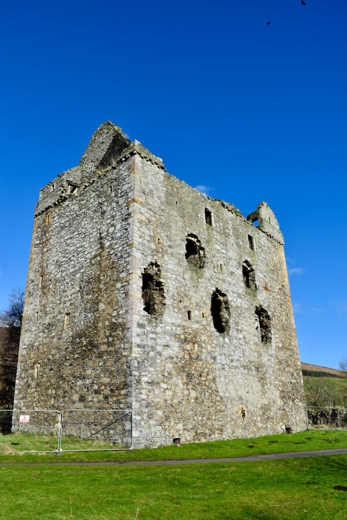 Close-up of tower, which looms above under a blue sky. Grey stonework prominent.