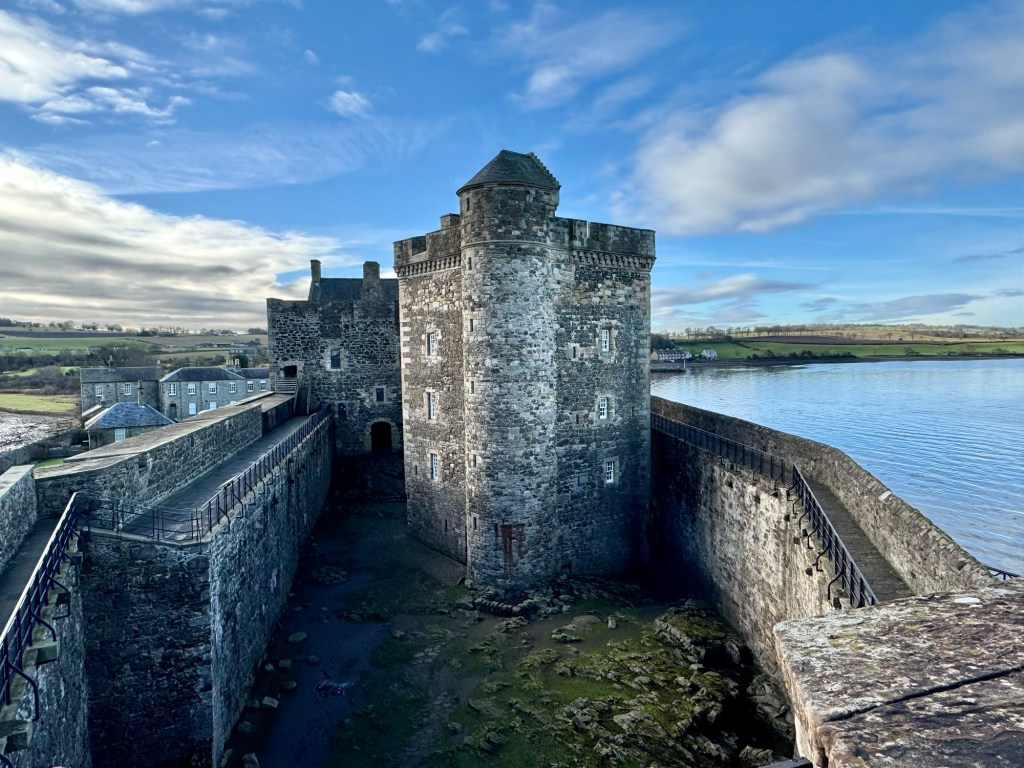 Looking back from the seaward point of the curtain wall. Courtyard below, then the prison tower with others behind.. Firth of Forth visible on the right, with distant green fields to the horizon.