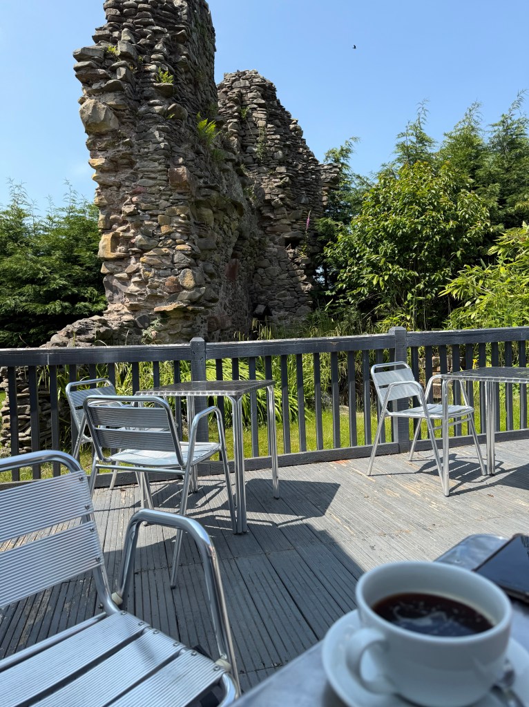 Cafe tables and chairs in foreground, with the tower behind, a few metres away. Trees cover the background.