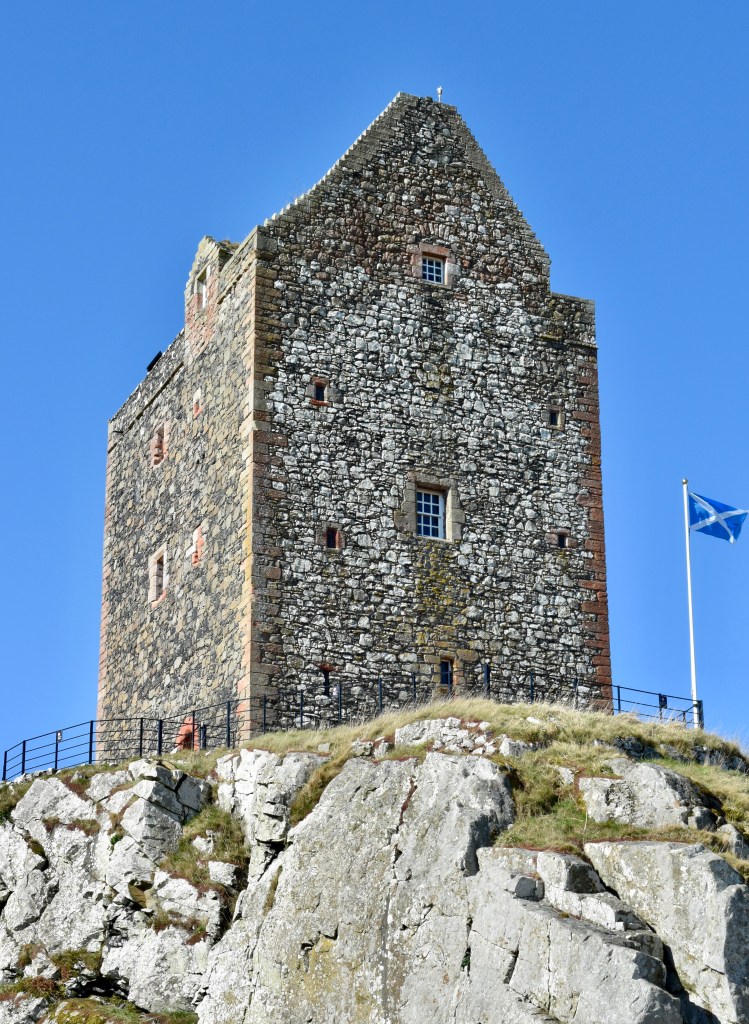 Looking up at the tower from the east. Two larger windows and some much smaller ones, in a stone facade, with a gabled roof. A saltire is flying on the right.