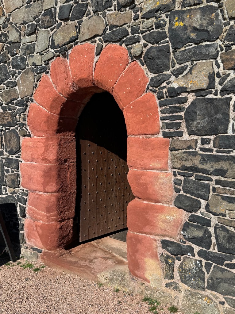 Close-up of the arched entrance, with the red sandstone of the archway, contrasting with the black stone of the building.