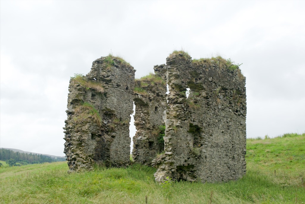 Looking up towards the tower, completely open at the front due to the missing wall. Garss growing on wall tops. Set against a grey sky.