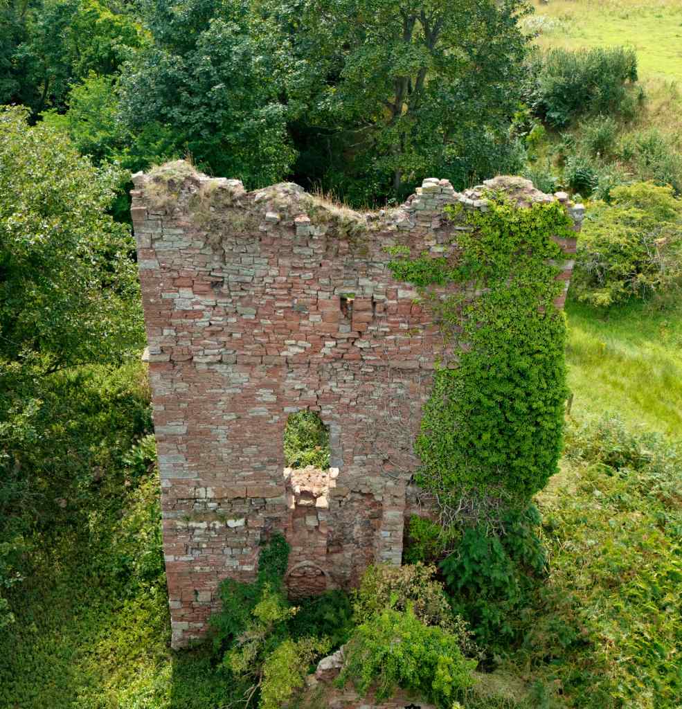Tower wall standing above two storeys. Damage along top and ivy growing up the right side to the top. Hole in centre above basement, may be the original entrance.
