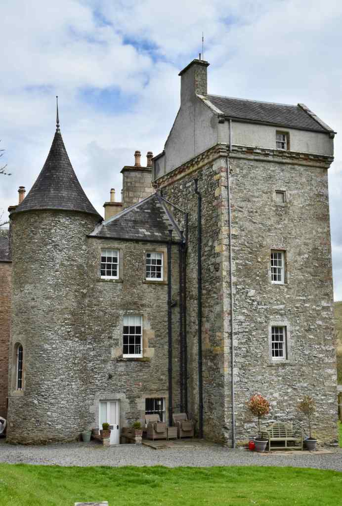 View of modernised castle, with 5-storey tower, including cap-house to the right, and smaller, narrower, turreted circular tower to the left. Seats in front of the building.