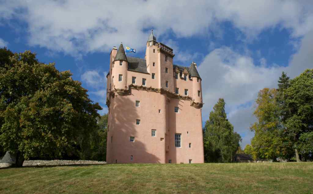 View from the east looking uphill. Turrets in either corner, with a taller central turret. The pink harling in the sunlight has taken an almost pinkish-brown hue.