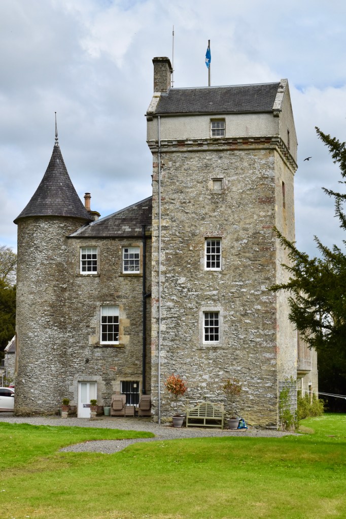 Portrait view from the west, Four-storey tower prominent on the right. with turreted smaller tower to the left. Grass in foreground.