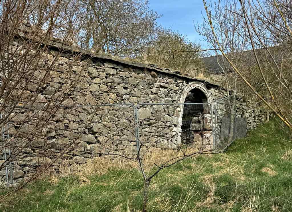 Almost complete section of wall with the arched entrance, just right of centre. Trees in foreground.