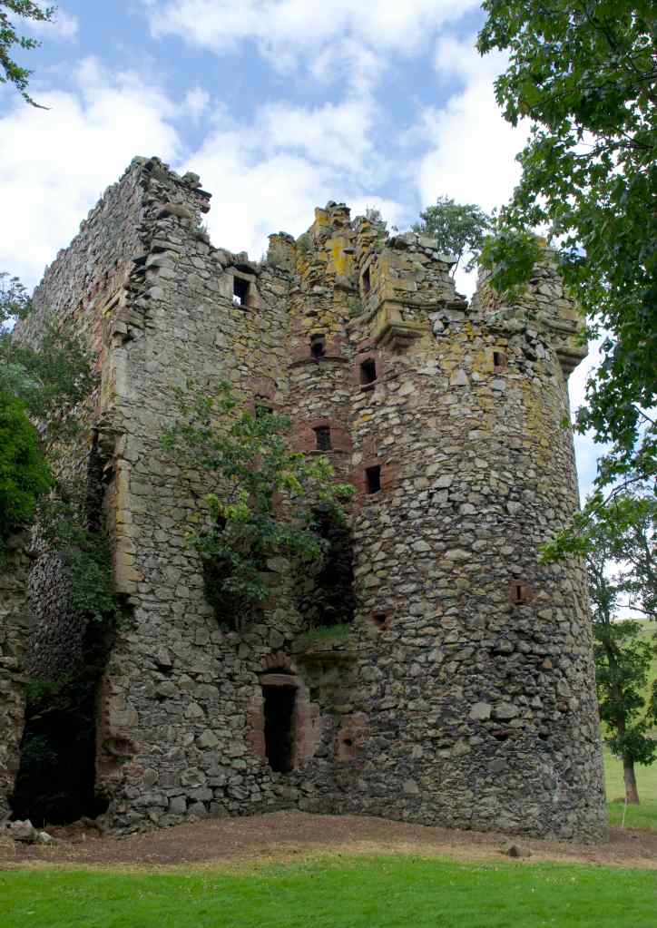 Castle standing almost to full height with circular tower extending from the wall on the right. Trees on either side and growing within the ruin.