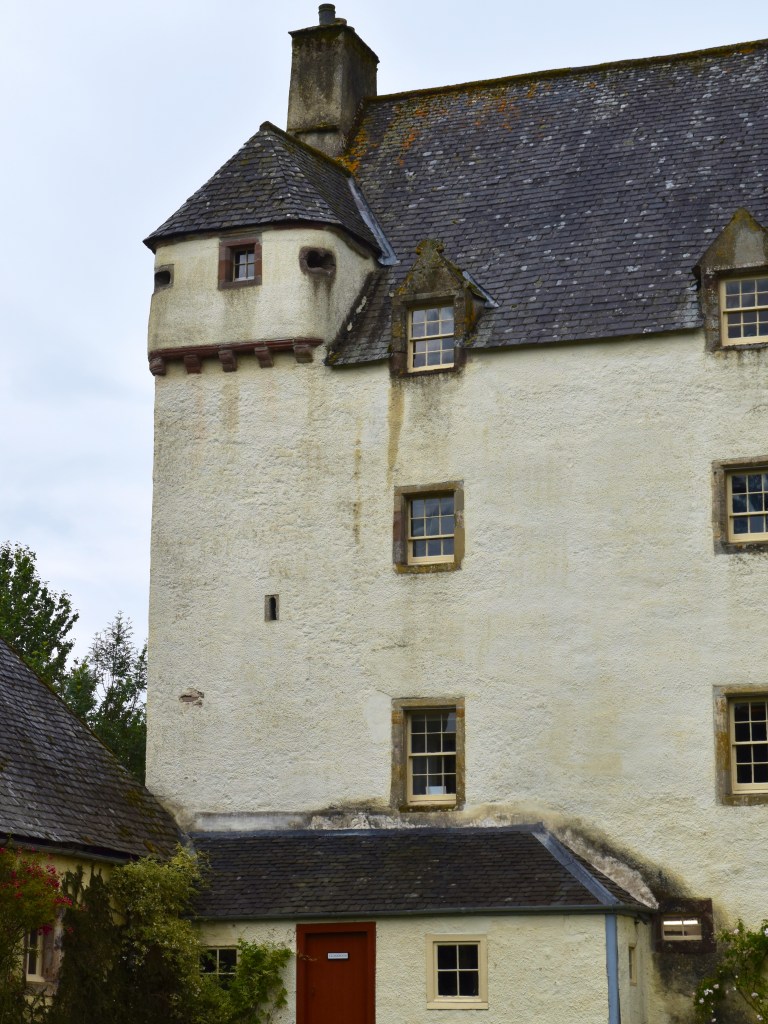 Left hand-side of the main block. White-harled facade, fading to cream. Small turret at the top with chimney stack beyond.