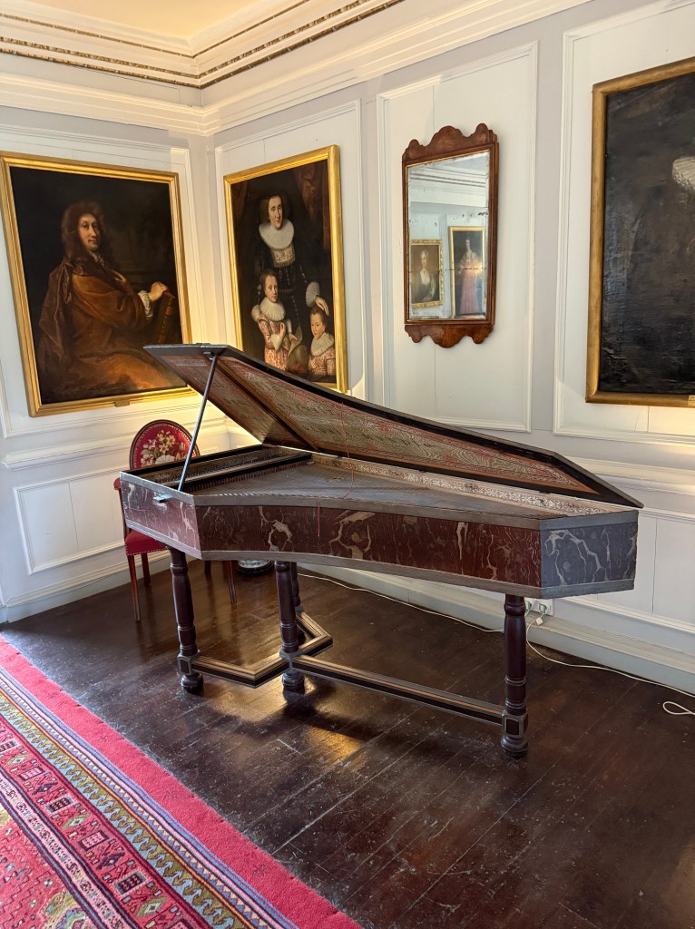 Dark wooden instrument, resembling a small piano, set in the corner of room under portrait paintings