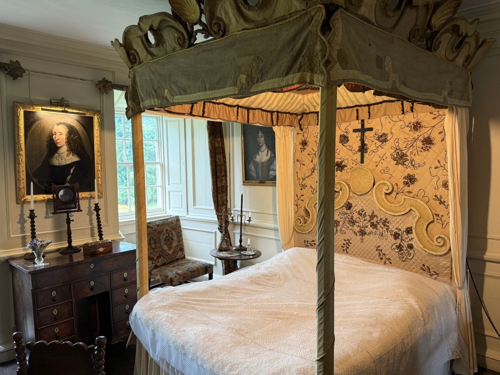 Four-poster bed with gold colour furnishings. Single window to left.