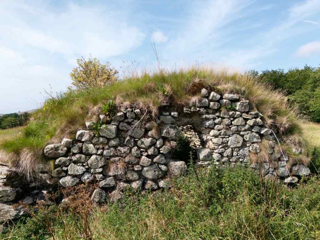 close-up of the basement end. Stones visible but showing signs of wear. Grass over the roof and to the sides and foreground.