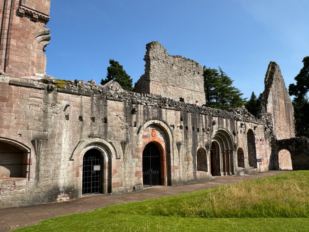 A series of arched entrances in a mostly single-storey structure. Taller elements to the rear and at the sides. Grass to the front.