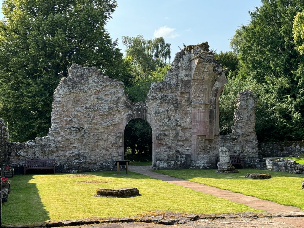Arched gateway with path, set in broken wall with trees behind.
