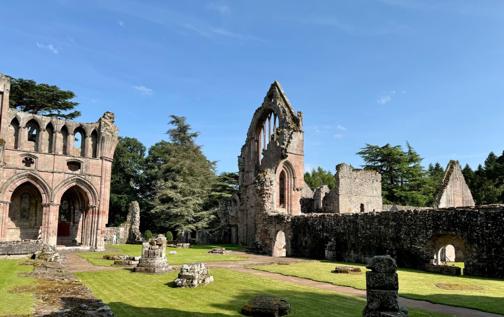 Ruined structures within manicured grass lawn. Arches visible on the left.