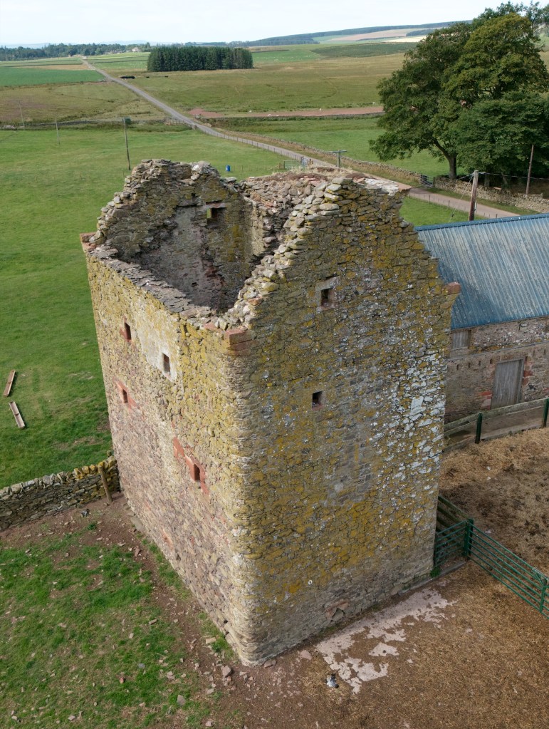 Drone image from south east, showing missing roof and attached farm building on right.