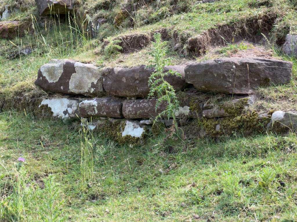 Three layers of weathered stones, energing from a grassy mound.