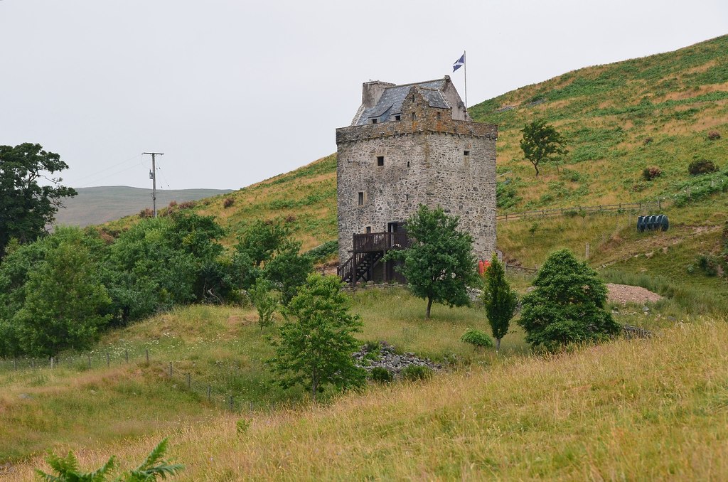The tower, flying a saltire from its flagpole, with the hill rising beyond. Small trees can be seen in the foreground.