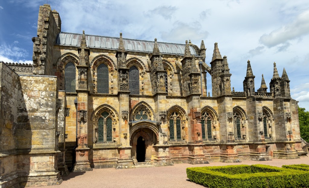 Side view with two levels of arched windows and small spires along the front between the windows. The church roof rises beyond.